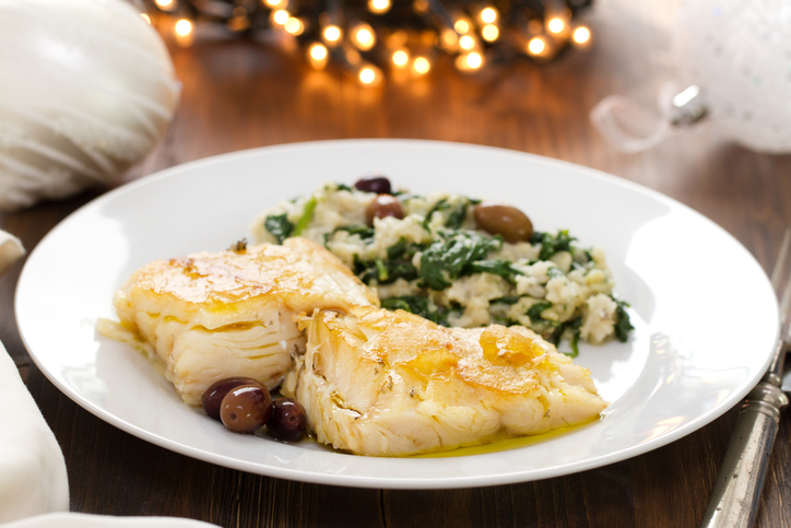 codfish with bread and spinach on white plate on brown wooden background