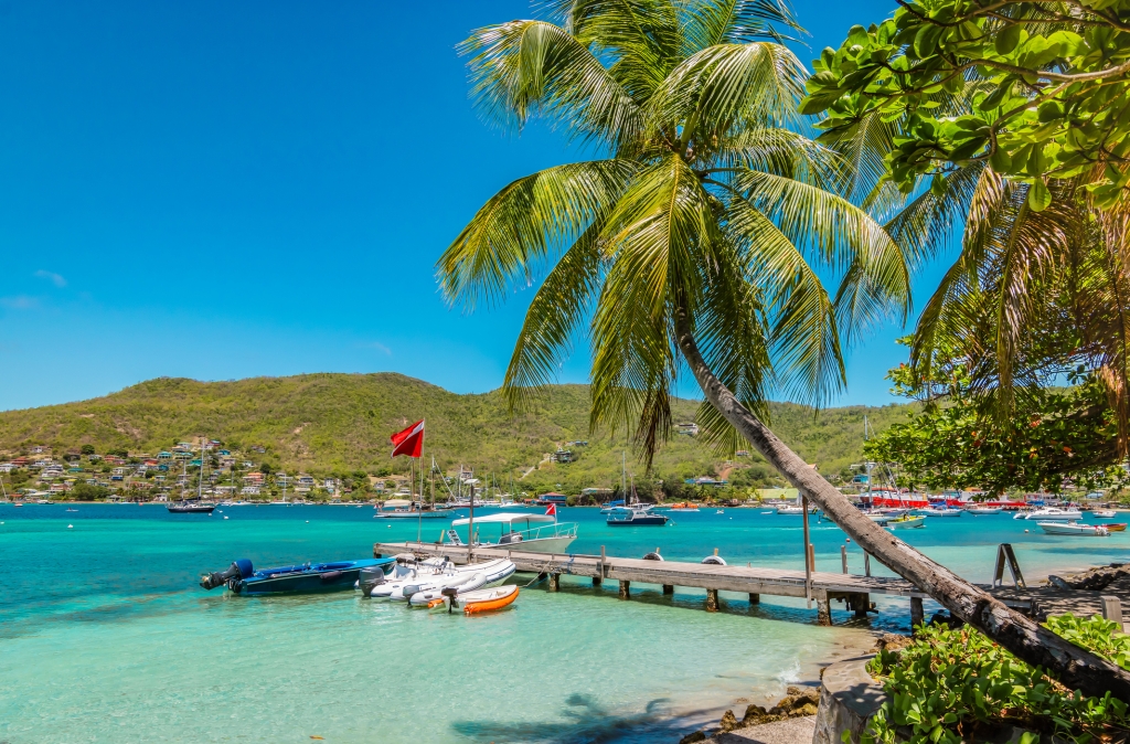 Bright and colorful image of Bequia. Palm trees at the water, blue sky and white clouds, boats in the harbor of Port Elisabeth. Saint Vincent and the Grenadines.