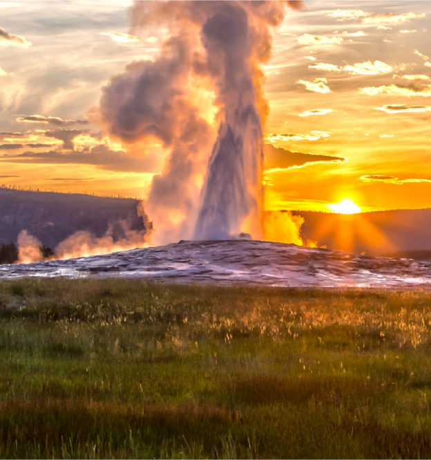 Old Faithful Geyser at Yellowstone National Park erupts at sunset.