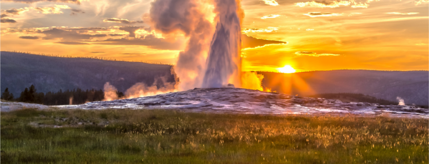 Old Faithful Geyser at Yellowstone National Park erupts at sunset.