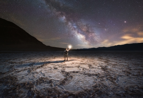 man holds a light up at night while viewing the milky way