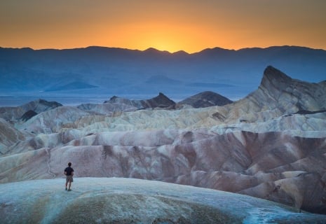 Classic panoramic view of male hiker standing at famous Zabriskie Point viewpoint in beautiful golden evening light at sunset in summer, Death Valley National Park, California, USA
