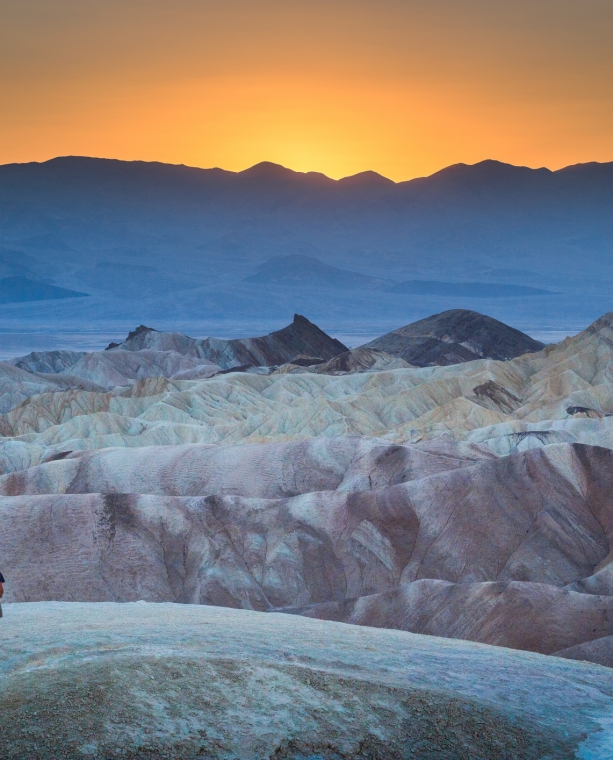 Classic panoramic view of male hiker standing at famous Zabriskie Point viewpoint in beautiful golden evening light at sunset in summer, Death Valley National Park, California, USA