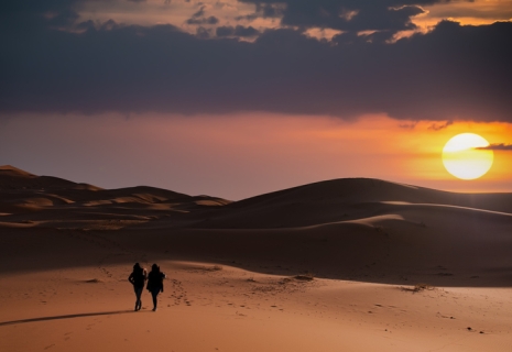 (Selective focus) Silhouette of two people walking on the sand dunes of the Merzouga desert during a stunning sunset. Merzouga, Morocco.