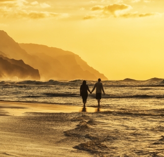 Silhouette of a couple at sunset walking along a Hawaiian beach.