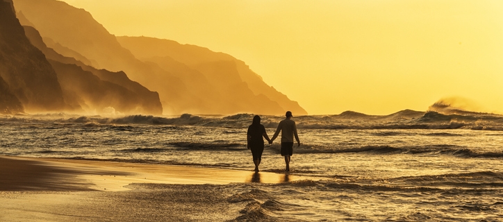 Silhouette of a couple at sunset walking along a Hawaiian beach.