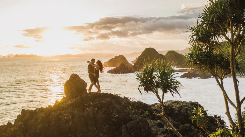 Couple enjoying sunset with amazing ocean and mountain view. Travel concept, panoramic shot, wanderlust.