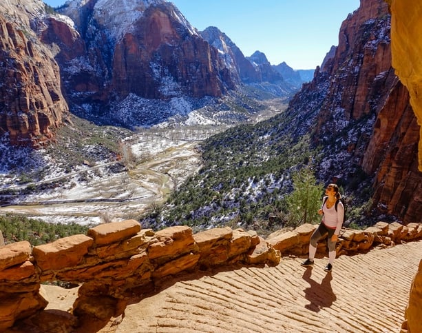 fit female traveler hikes along the angel's landing hiking path on a sunny winter day. woman visiting zion national park observes the spectacular wintry canyon while walking along a scenic trail.