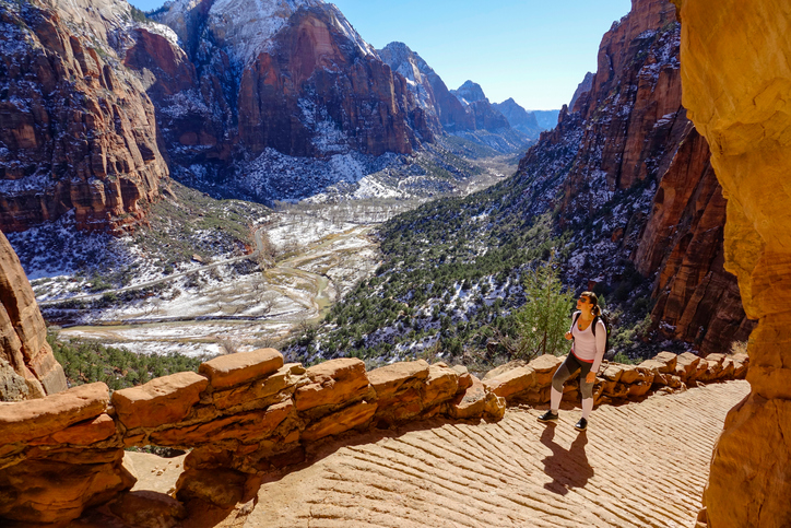 fit female traveler hikes along the angel's landing hiking path on a sunny winter day. woman visiting zion national park observes the spectacular wintry canyon while walking along a scenic trail.