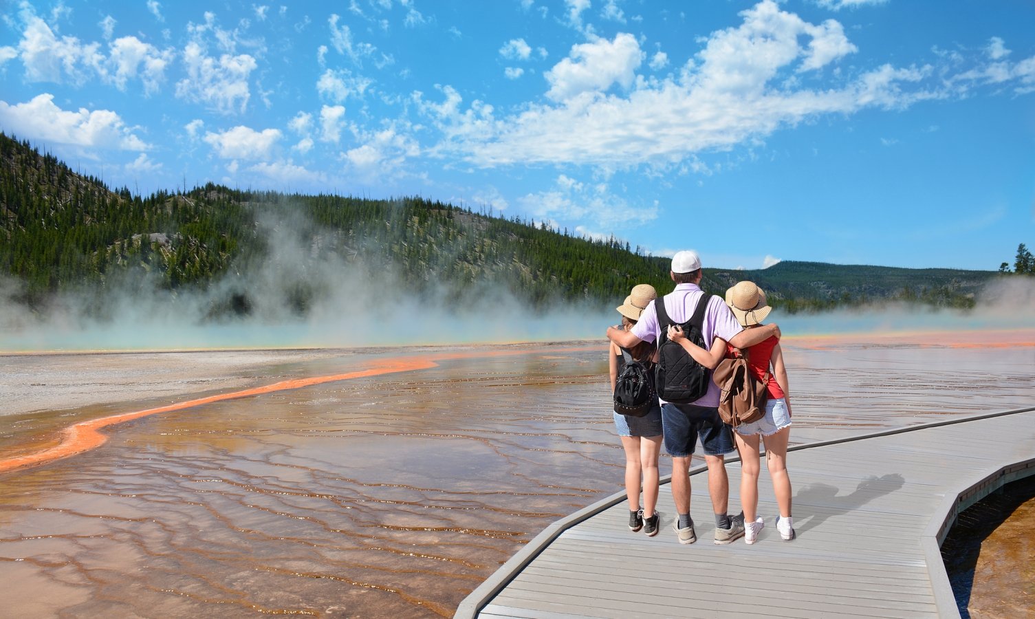 Family hiking on vacation, standing with arms around, , looking at beautiful gazer. Blue sky in the background. Midway Geyser Basin, Grand Prismatic Spring, Yellowstone National Park, USA,